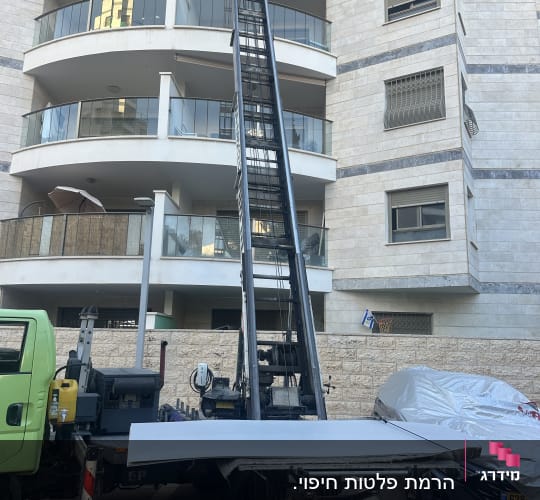 מנוף הרמה מחובר למשאית ליד בניין מגורים